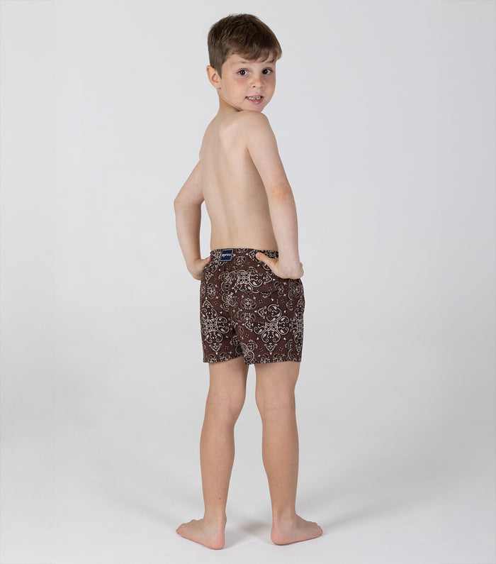 brown bandana Young boy wearing patterned swim shorts on a white background