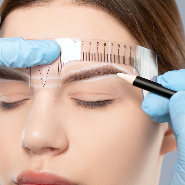Woman getting eyebrows shaped using an eyebrow stencil and white brow pencil