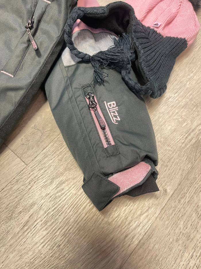 Close-up of Blizz girls snowsuit sleeve showing adjustable cuff, zipper pocket, and winter fabric details.
