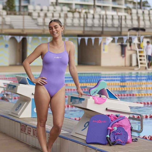 Amani Girls Iris Proback One Piece Swimsuit in purple, featuring a stylish back design, perfect for swimming and beach wear.