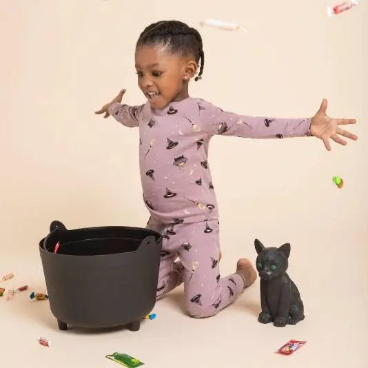 Girl playing in Petit Lem Bewitched glow-in-the-dark pajamas with Halloween-inspired witch print.