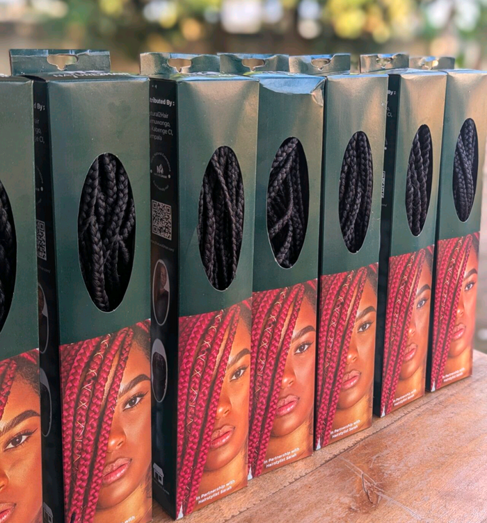 [color:Black] Several boxes of black braided hair extensions arranged in a row on a wooden surface, with oval cutouts showing the black braids inside and printed model photos on the front.