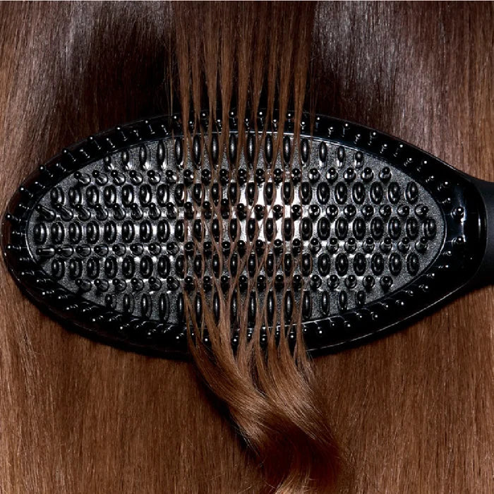 Black hairbrush with brown hair being brushed on a wooden surface