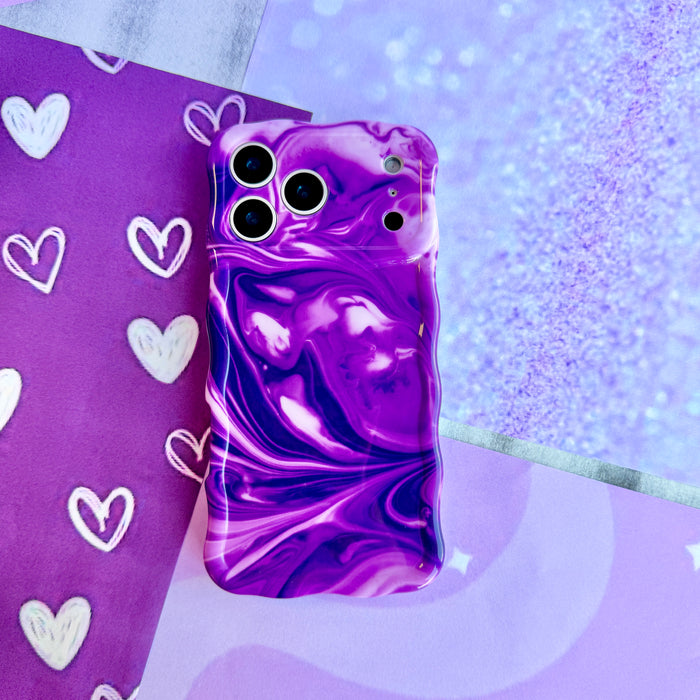 Grape Crush Wavy Luxe MagSafe iPhone case styled on a purple heart print backdrop, showing the glossy swirled purple and white marble finish.