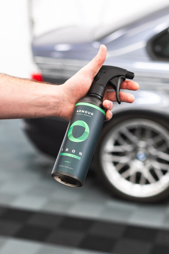 A closeup of a person holding a spray bottle of Armour Iron.