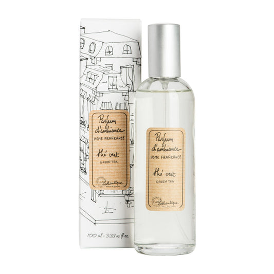 A clear glass room spray bottle with a label next to its packaging featuring a drawing of a house.