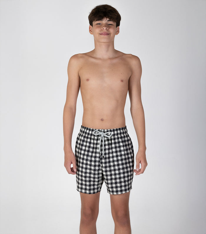 gingham Young boy wearing black and white checkered shorts on a plain background