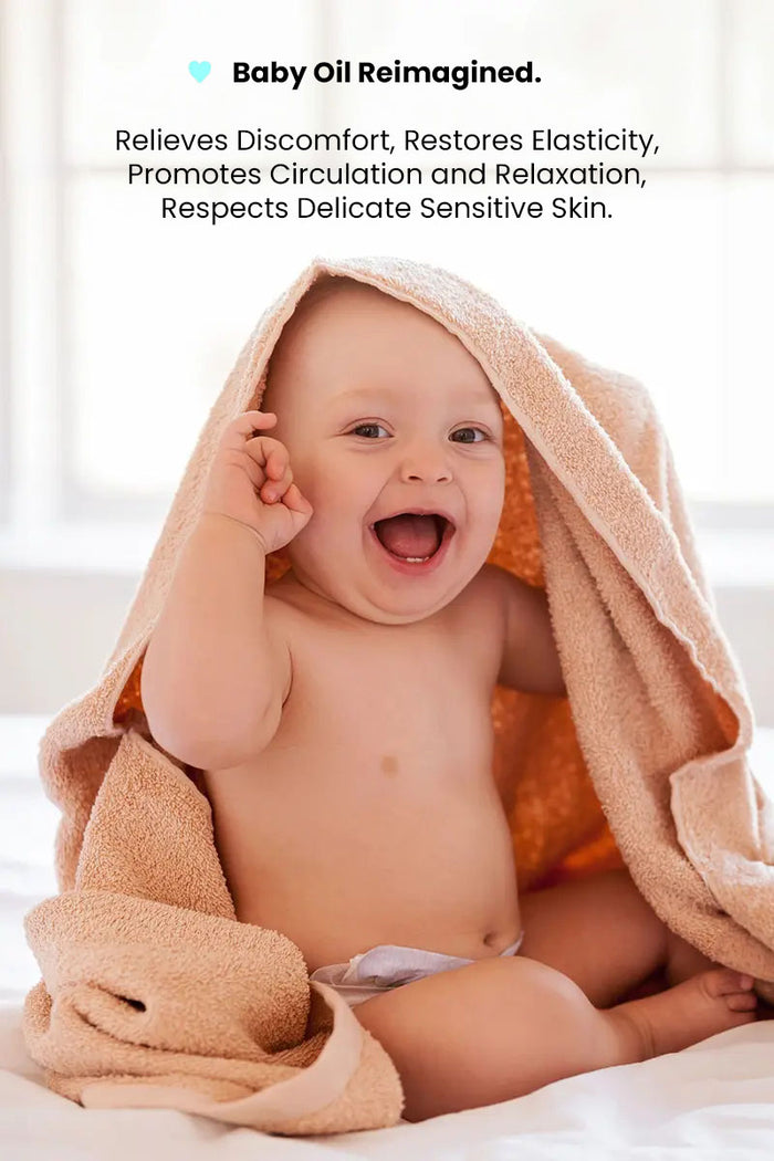 happy baby smiling after a massage with a towel on head and text reading "baby oil reimagined, relieves discomfort, restores elasticity, promotes circulation and relaxation, respects delicate sensitive skin".