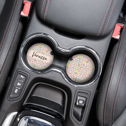 Two round car coasters with personalised names and a ditsy flower meadow pattern in pastel colours.