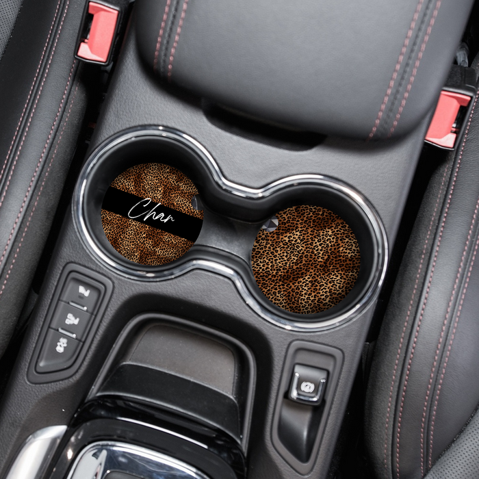 Leopard print car coaster with custom name Char in a black car interior with red trim.
