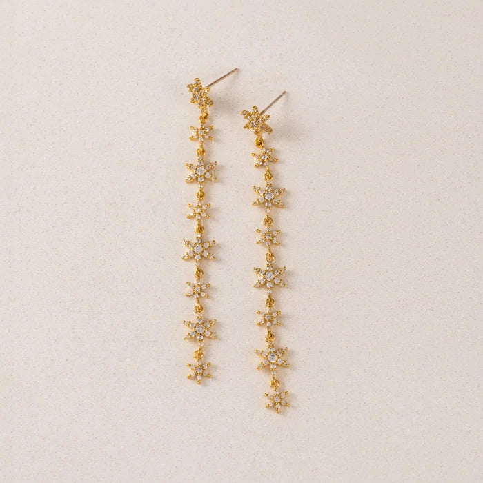 Gold floral earrings on a beige background