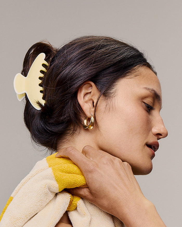 Woman with a yellow hair clip in her hair, wearing gold earrings, against a neutral background.