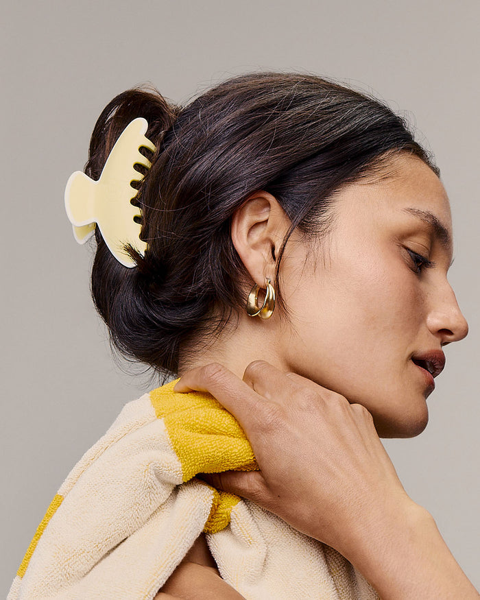 Woman with a yellow hair clip and towel, wearing gold earrings, against a neutral background