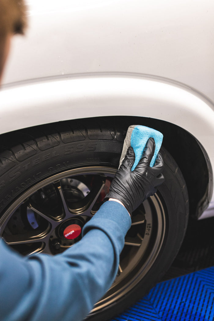 Person cleaning a car tire with a blue sponge and black gloves.