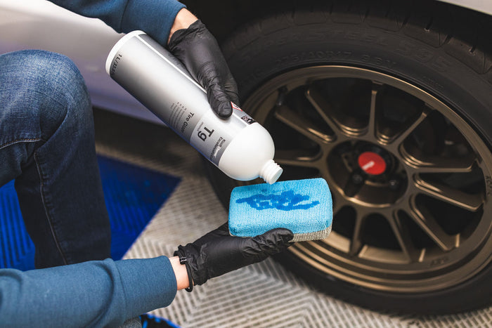 Person cleaning a car's tire with KochChemie Tire Glaze on a blue applicator.
