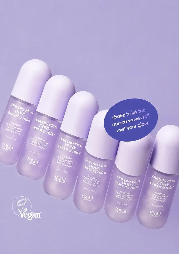 Six small roll-on bottles of Tangle Teezer Imply Eco Formula Hair Mist arranged diagonally on a light lavender background, with a blue circular callout and a white vegan logo.