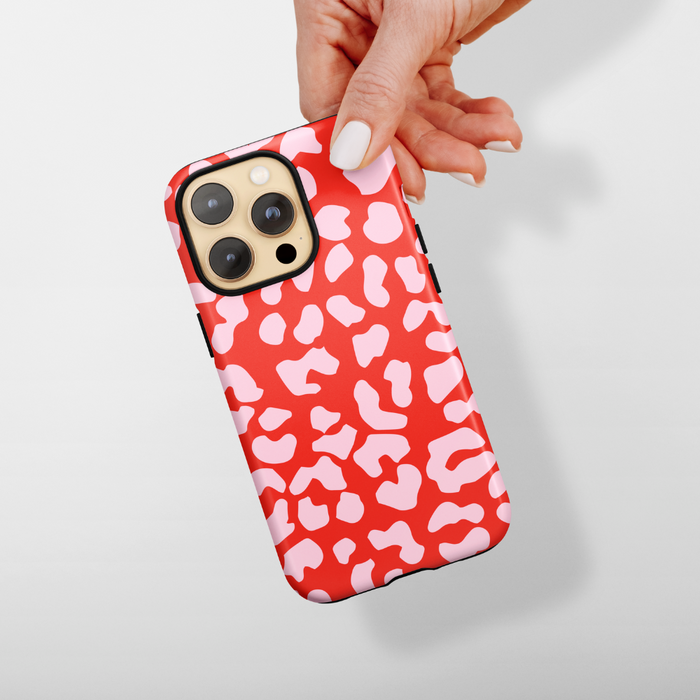 Hand holding a Coconut Lane Tough MagSafe phone case with a red and pink abstract leopard print pattern.