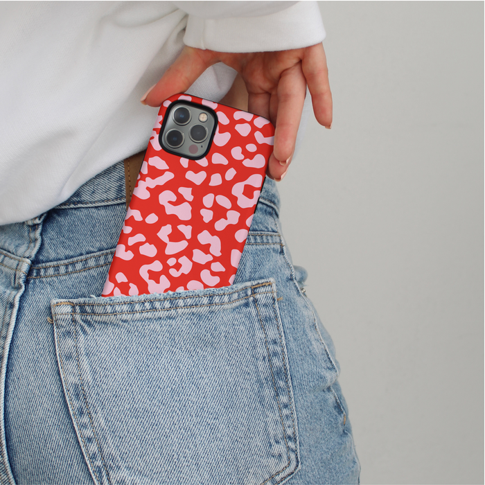 Red and pink leopard print phone case being slid into the back pocket of blue jeans by a hand.