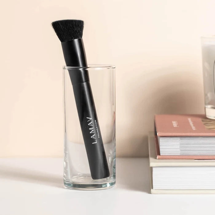 LAMAV foundation brush in a glass on a desk with books to the side.