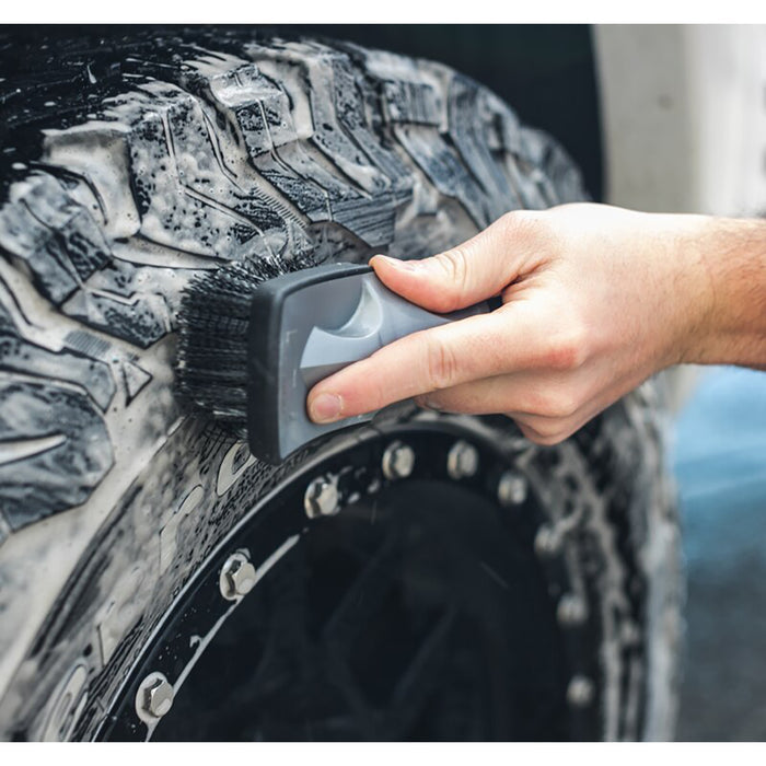 A closeup of a person scrubbing a tire with a Tire Brush.