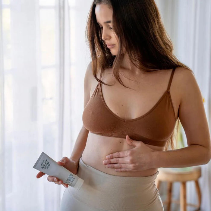 Woman applying cream to her stomach with a bottle of wild yam cream in a bright room.