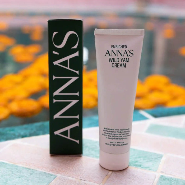 Tube and box of Anna's Enriched Wild Yam Cream on a colorful surface with blurred flowers in the background.