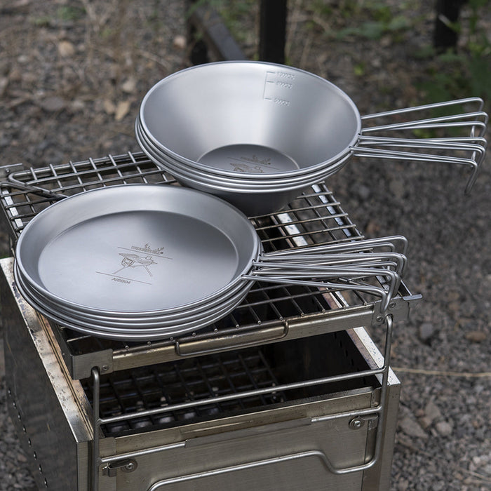 Winnerwell® stainless steel Sierra cooking bowls and plates placed on an outdoor grill, ready for campfire cooking.